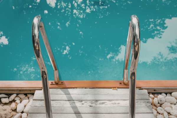 Pool deck steps with chrome handrails leading into a clear blue swimming pool, highlighting the importance of maintenance and resurfacing for safety and aesthetics. Pool deck steps with chrome handrails leading into a clear blue swimming pool, highlighting the importance of maintenance and resurfacing for safety and aesthetics.