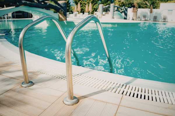 Pool deck with stainless steel handrails leading into clear turquoise water, illustrating a well-maintained swimming pool environment relevant to resurfacing services.