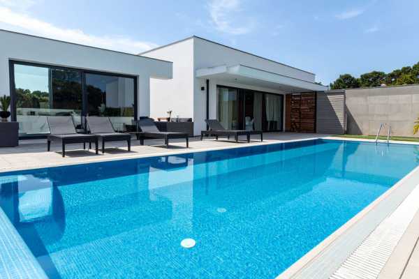 Modern swimming pool with lounge chairs beside a sleek, contemporary home, emphasizing energy efficiency and outdoor relaxation.
